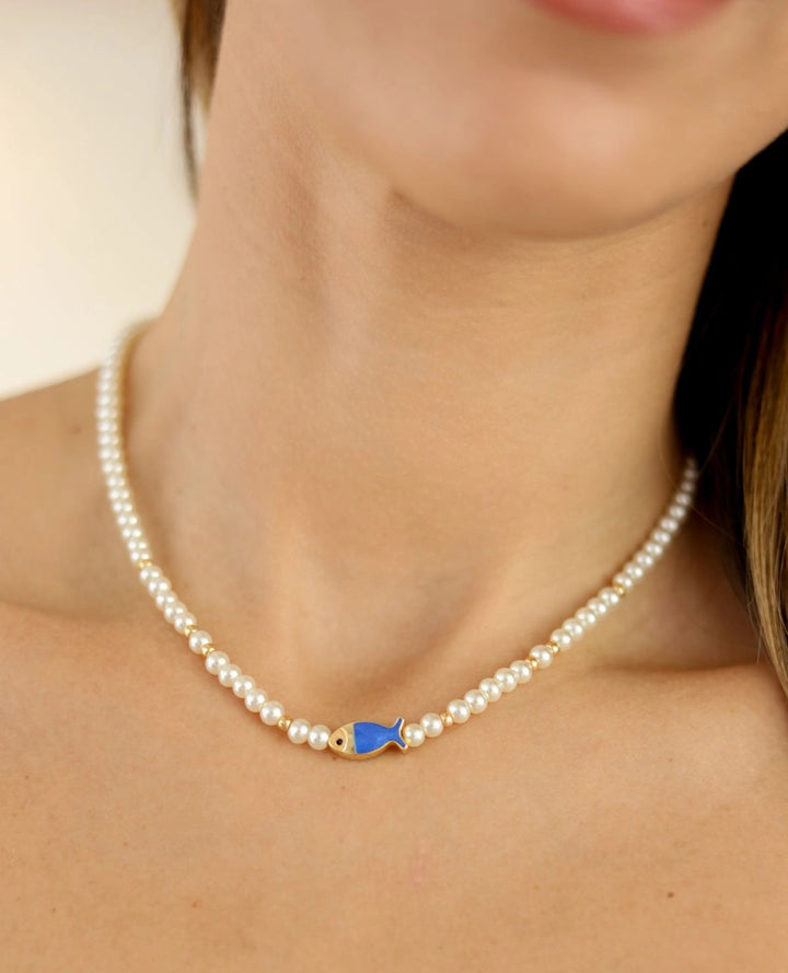 Pearl necklace with a blue fish pendant on a person's neck