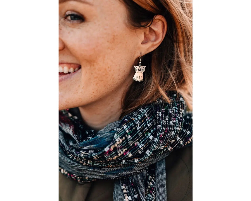 Woman wearing a patterned scarf and kitty-shaped earrings on a white background