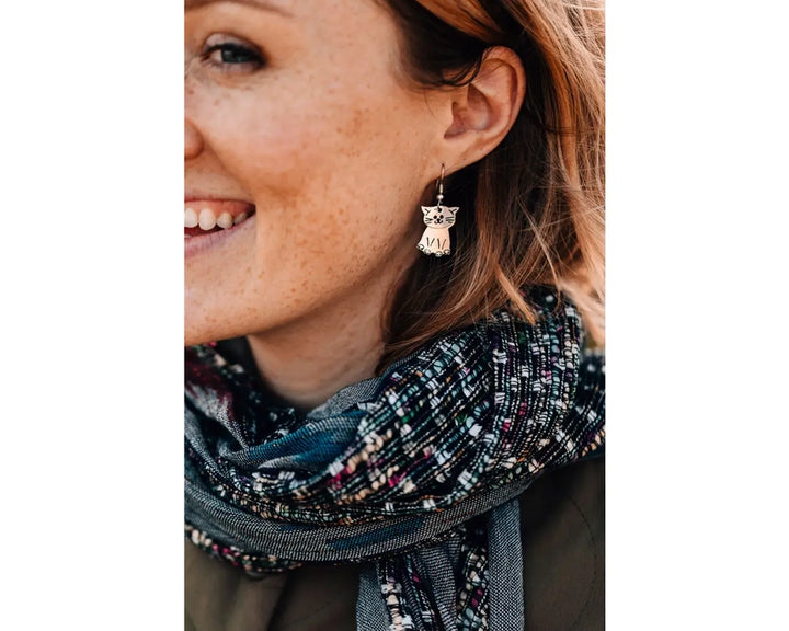 Woman wearing a patterned scarf and kitty-shaped earrings on a white background
