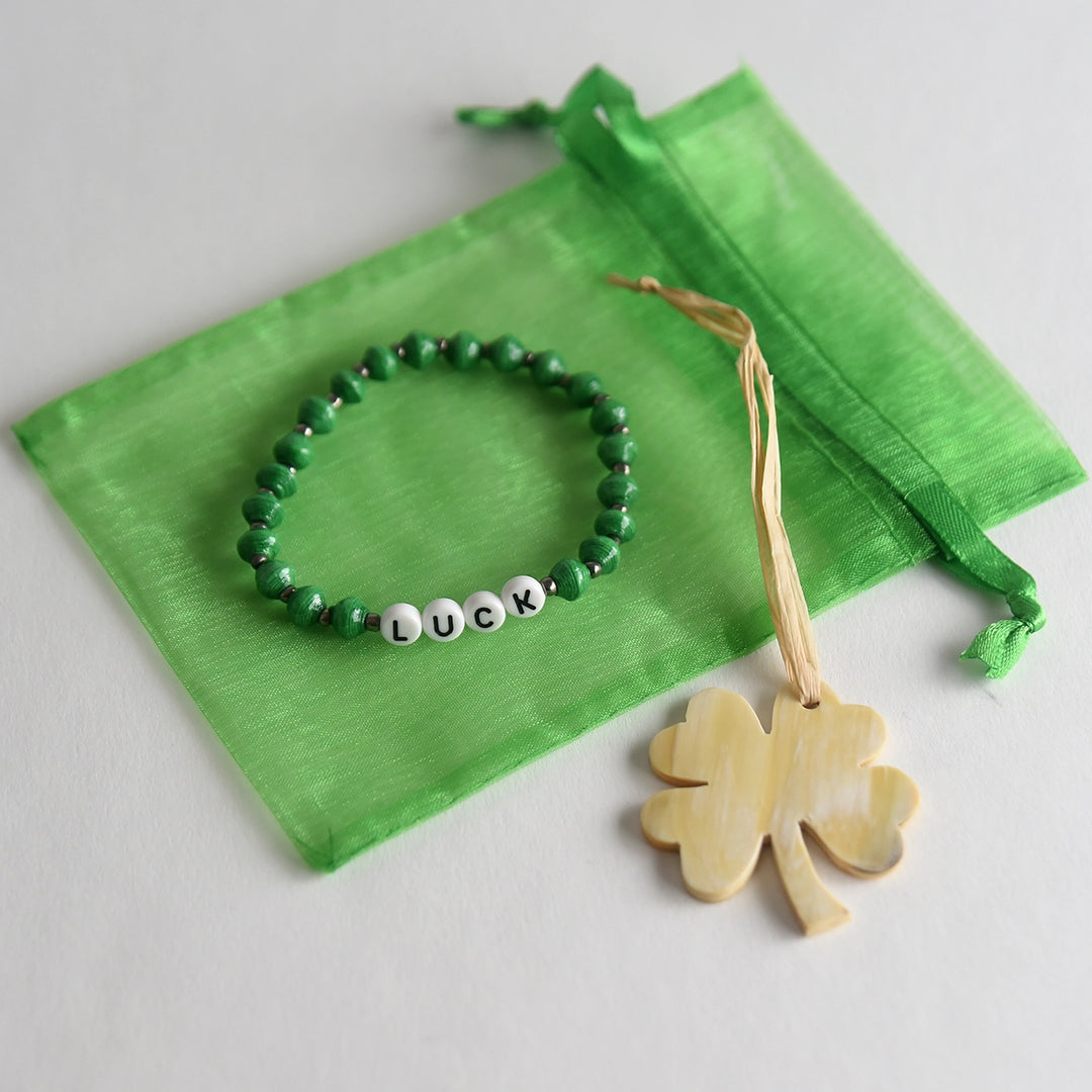 Green beaded bracelet with 'LUCK' beads on a green drawstring bag, accompanied by a wooden shamrock ornament.