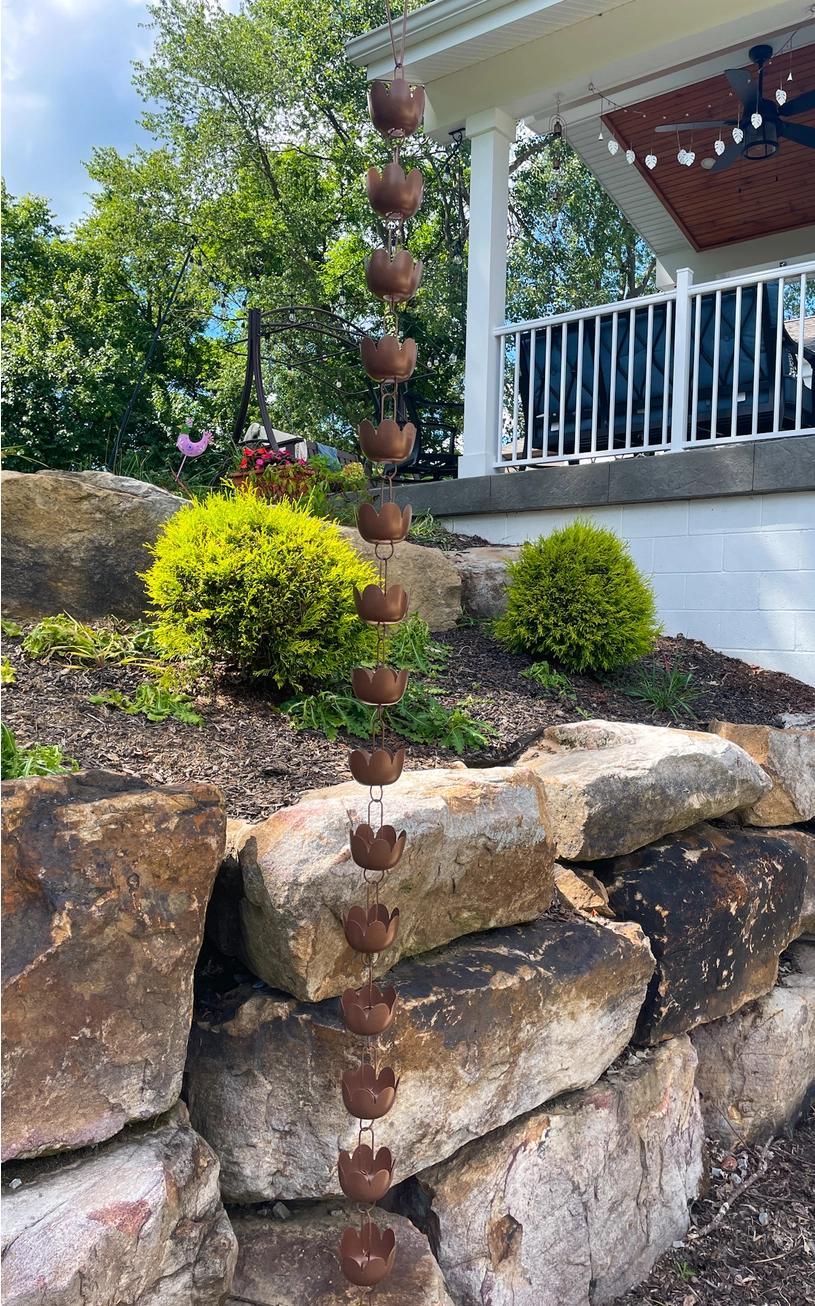 Decorative rain chain on a stone wall with a gazebo and garden in the background