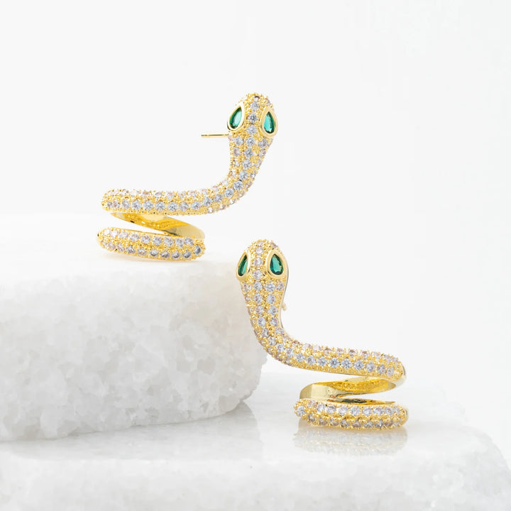Gold snake-shaped earrings with green eyes on a white background