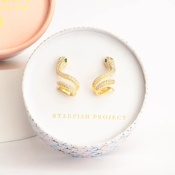 Gold snake-shaped earrings in a 'Starfish Project' box on a white background