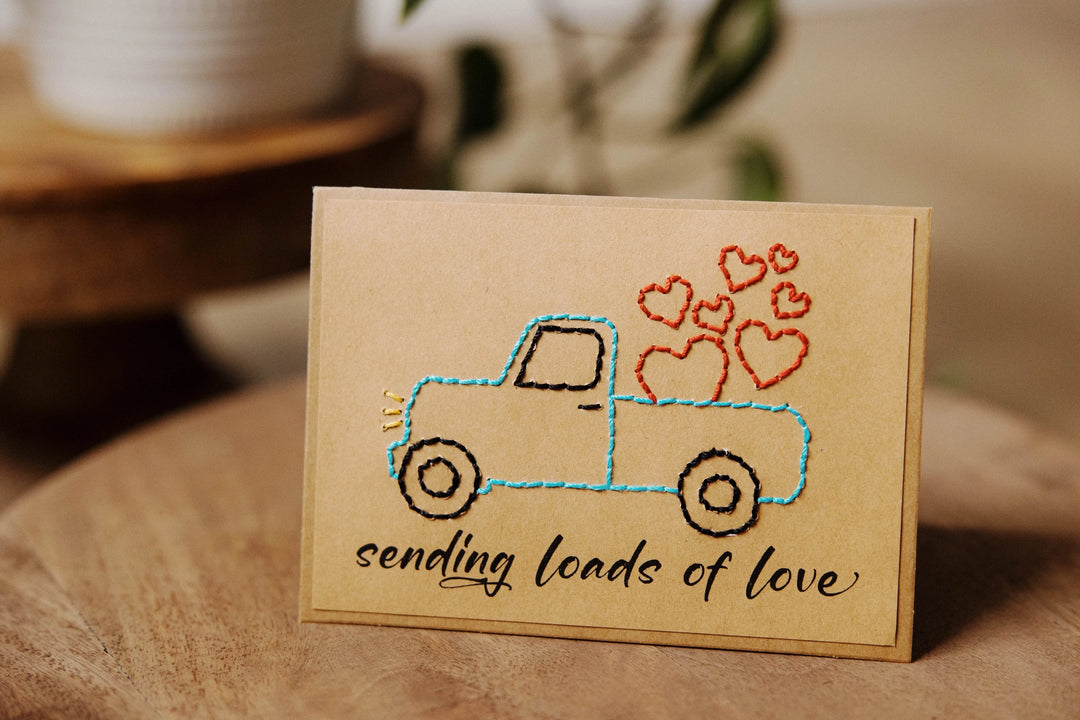 Card with embroidered truck and hearts design on a wooden surface