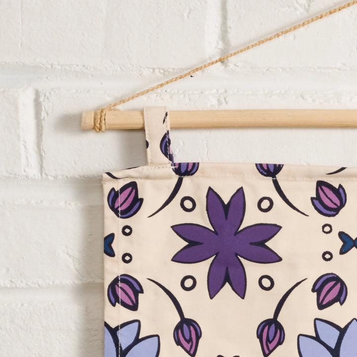 Floral patterned banner with purple flowers hanging on a white brick wall.