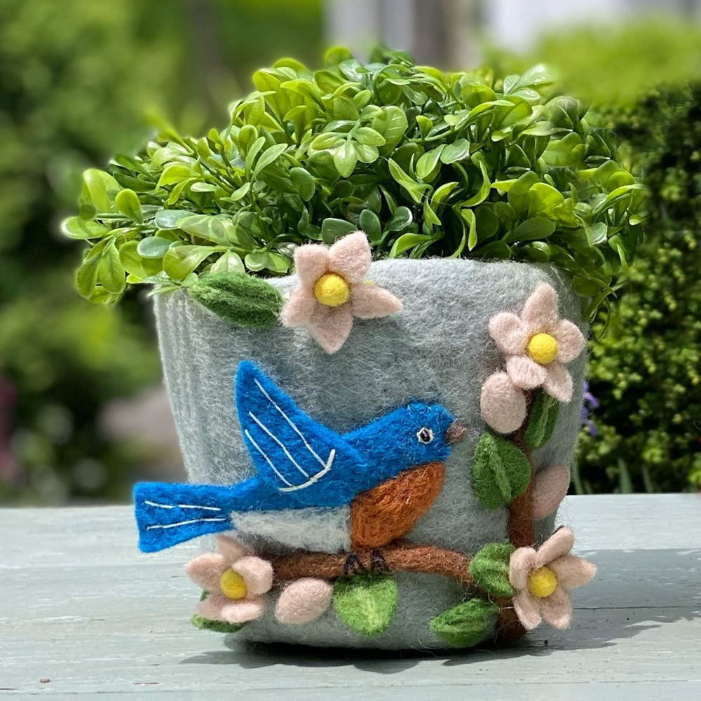 Decorative planter with a blue bird and flowers on a wooden surface