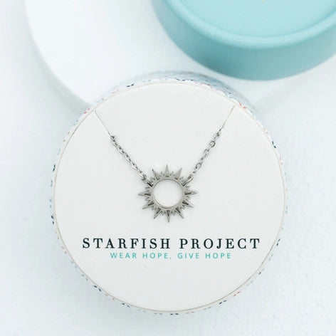 Starfish Project necklace on a white surface with a branded box in the background