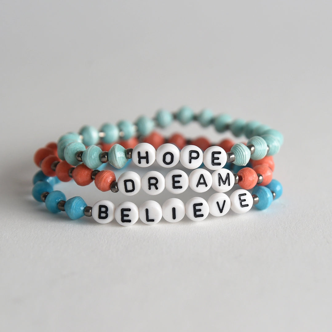 Stack of colorful beaded bracelets with motivational word beads on a light gray background