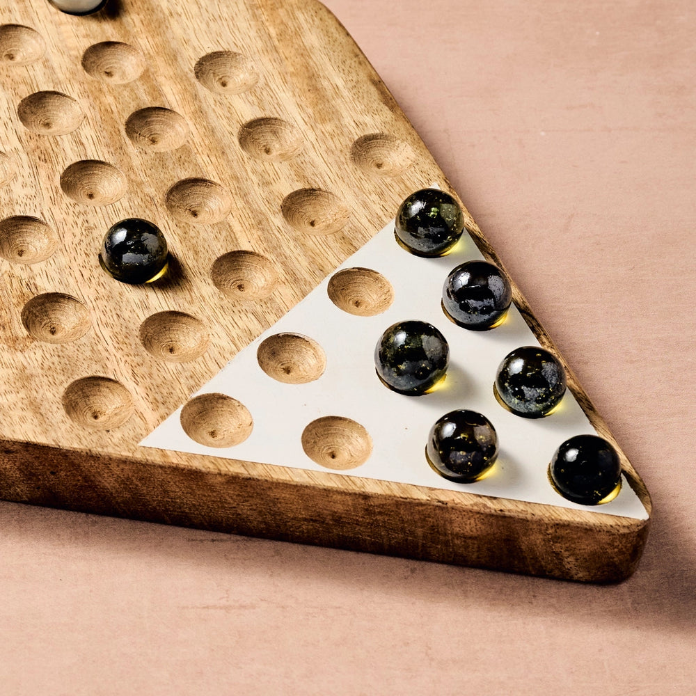 Wooden Chinese Checkers game board with black marbles on a beige background