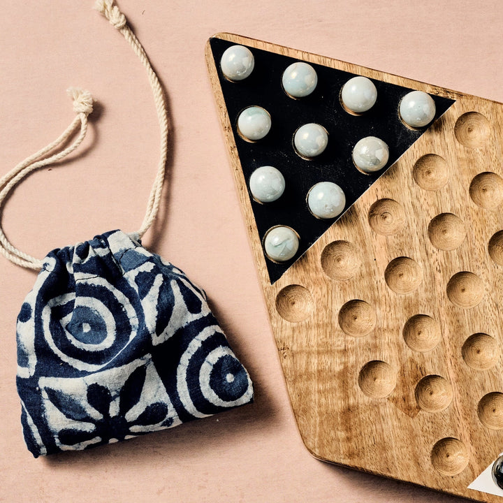 Wooden Chinese Checkers game with marble pieces and a patterned drawstring bag on a beige background