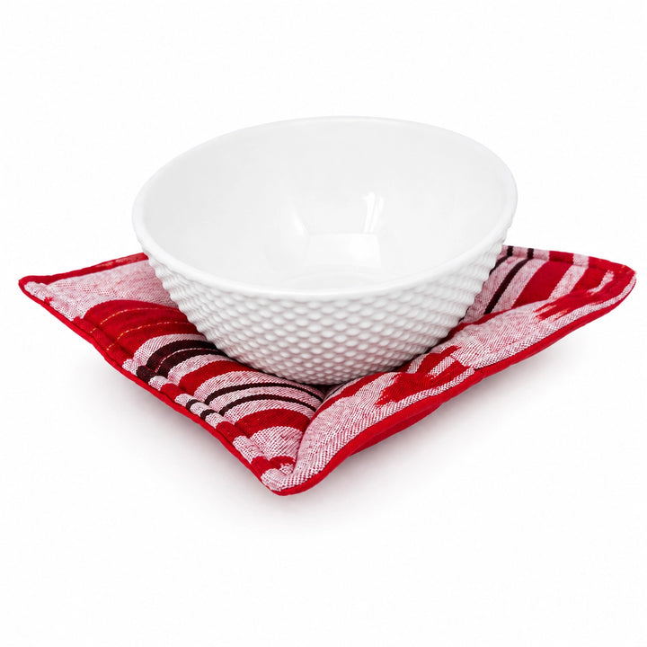 A white textured ceramic bowl resting on a red and white patterned bowl cozy, photographed on a clean white background.
