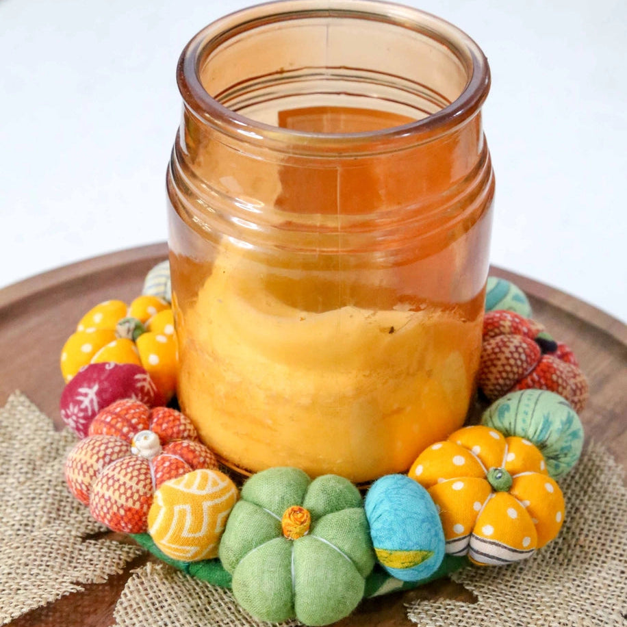 Candle in a glass jar with decorative pumpkins on a wooden surface