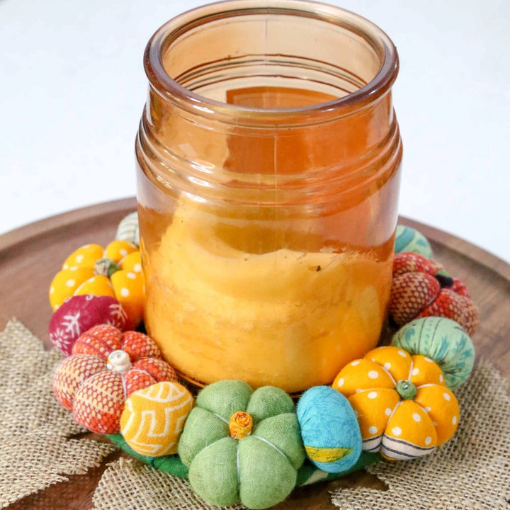 Candle in a glass jar with decorative pumpkins on a wooden surface