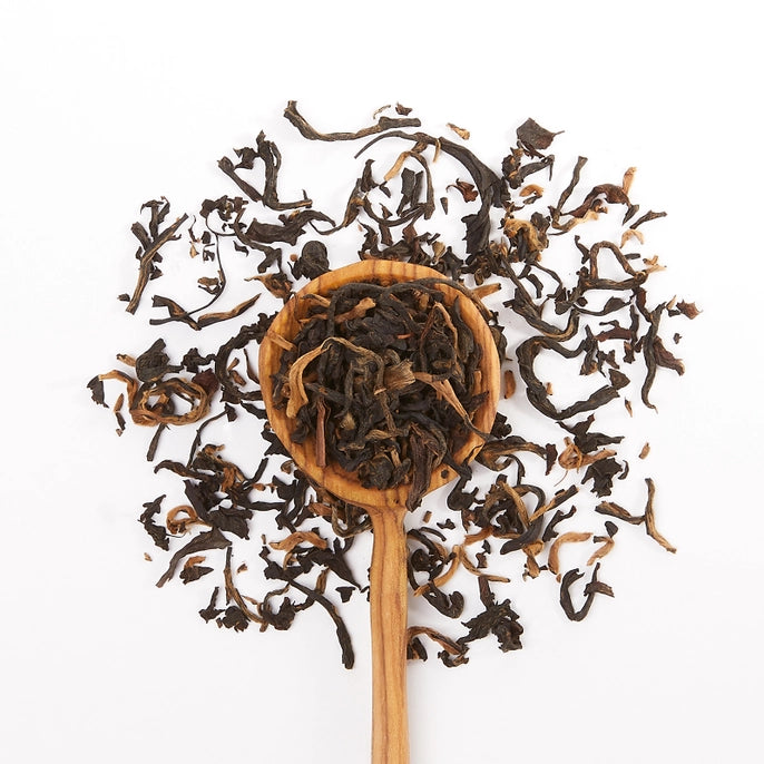 Wooden spoon filled with Nandi gold tea leaves on a white background