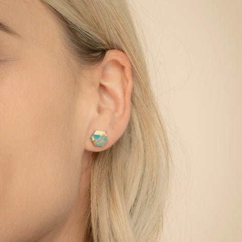 Close-up of a person wearing a gold earring with a blue gemstone on a beige background