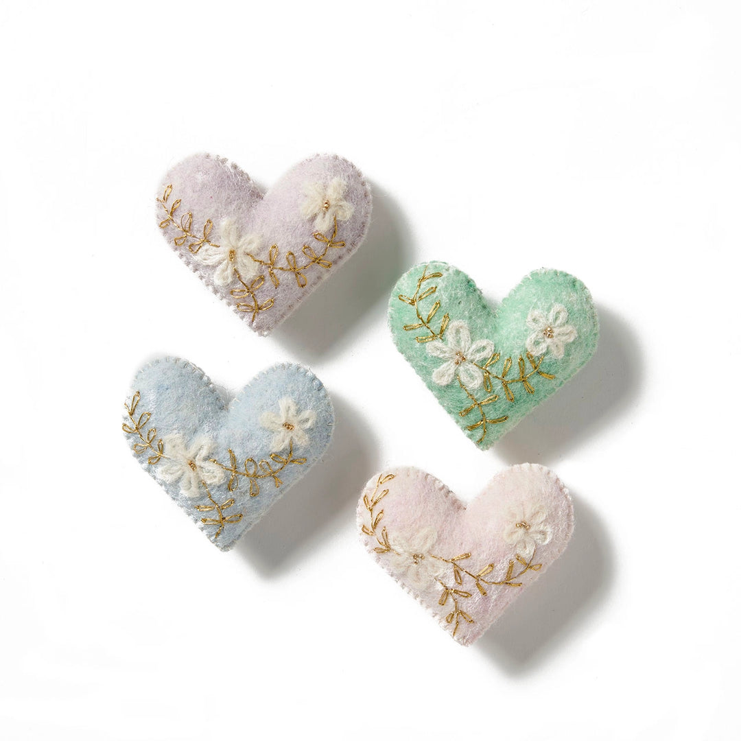 Four embroidered heart-shaped cushions in pastel colors on a white background