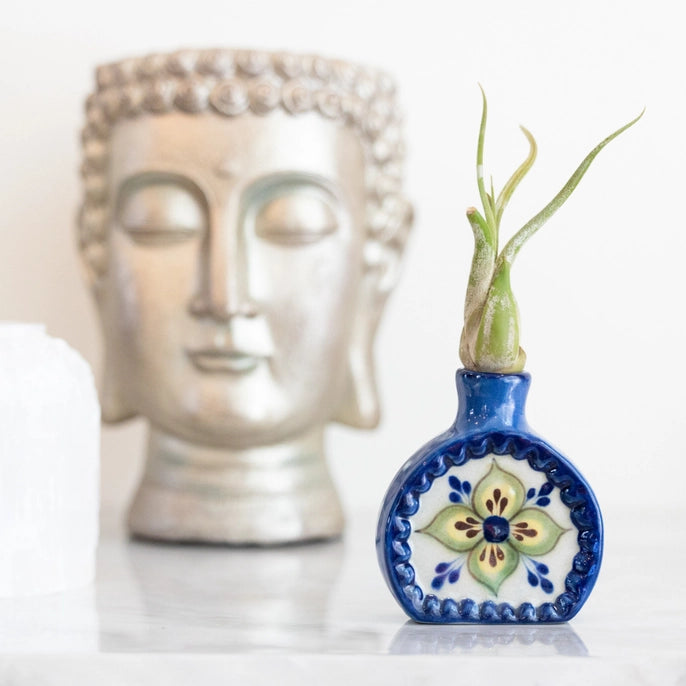 Decorative blue vase with floral design containing a plant, placed in front of a Buddha statue.