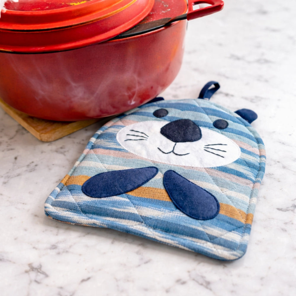Blue otter-shaped pot holder on a marble surface with a red pot in the background.
