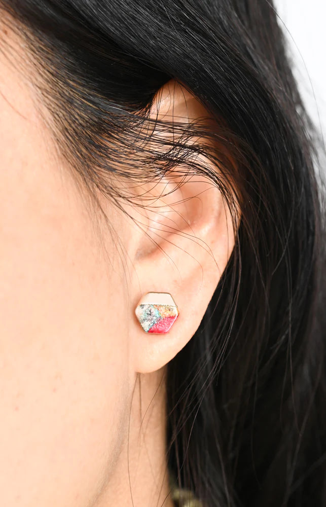 Close-up of an ear wearing a hexagonal earring with a colorful gemstone.
