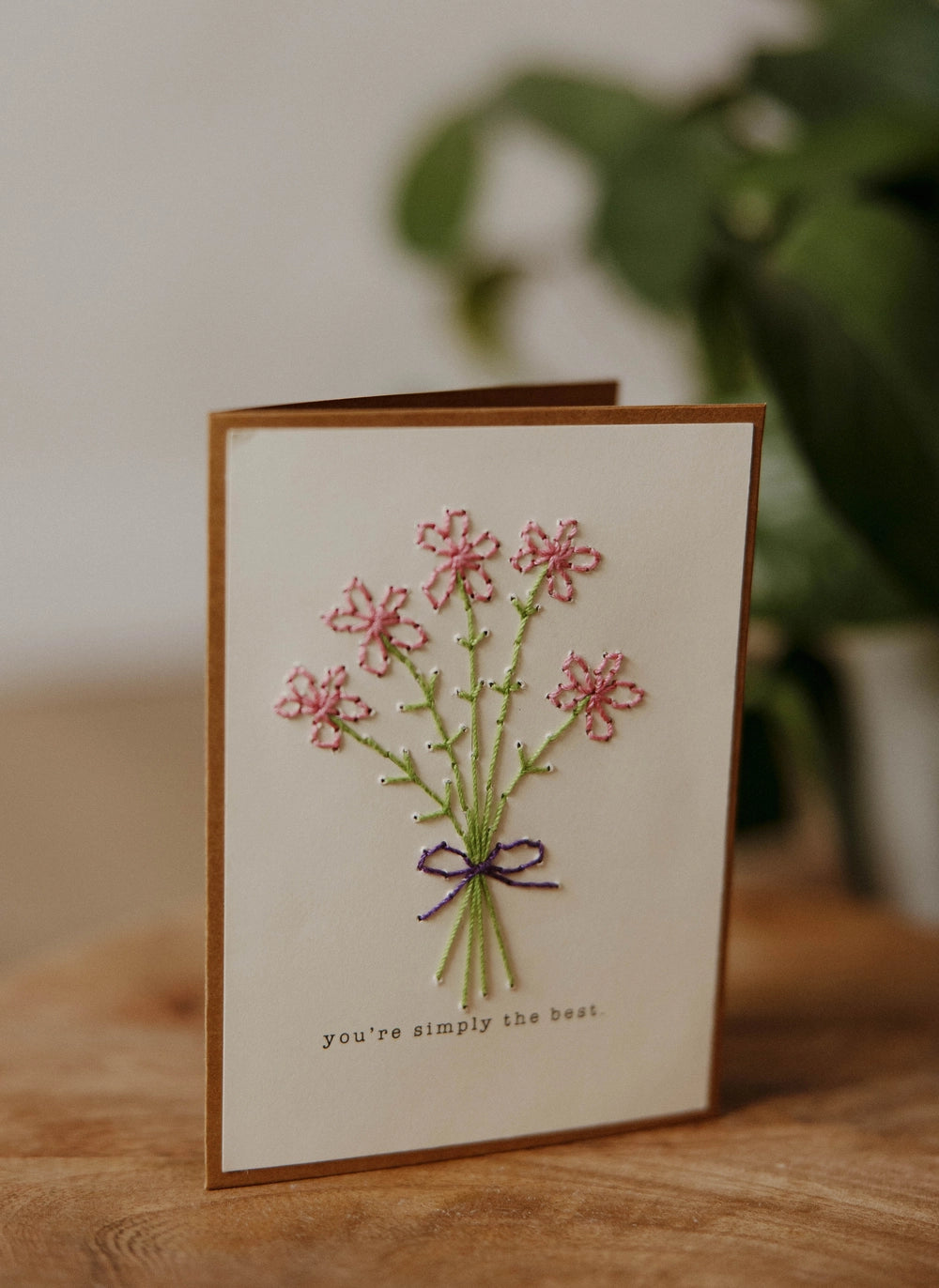 greeting card with pink flower bouquet tied with purple ribbon.  Card says "you're simply the best." 