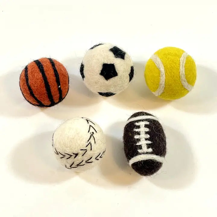 Five small felt sports balls on a plain white background, including basketball, soccer, tennis, baseball, and football designs.