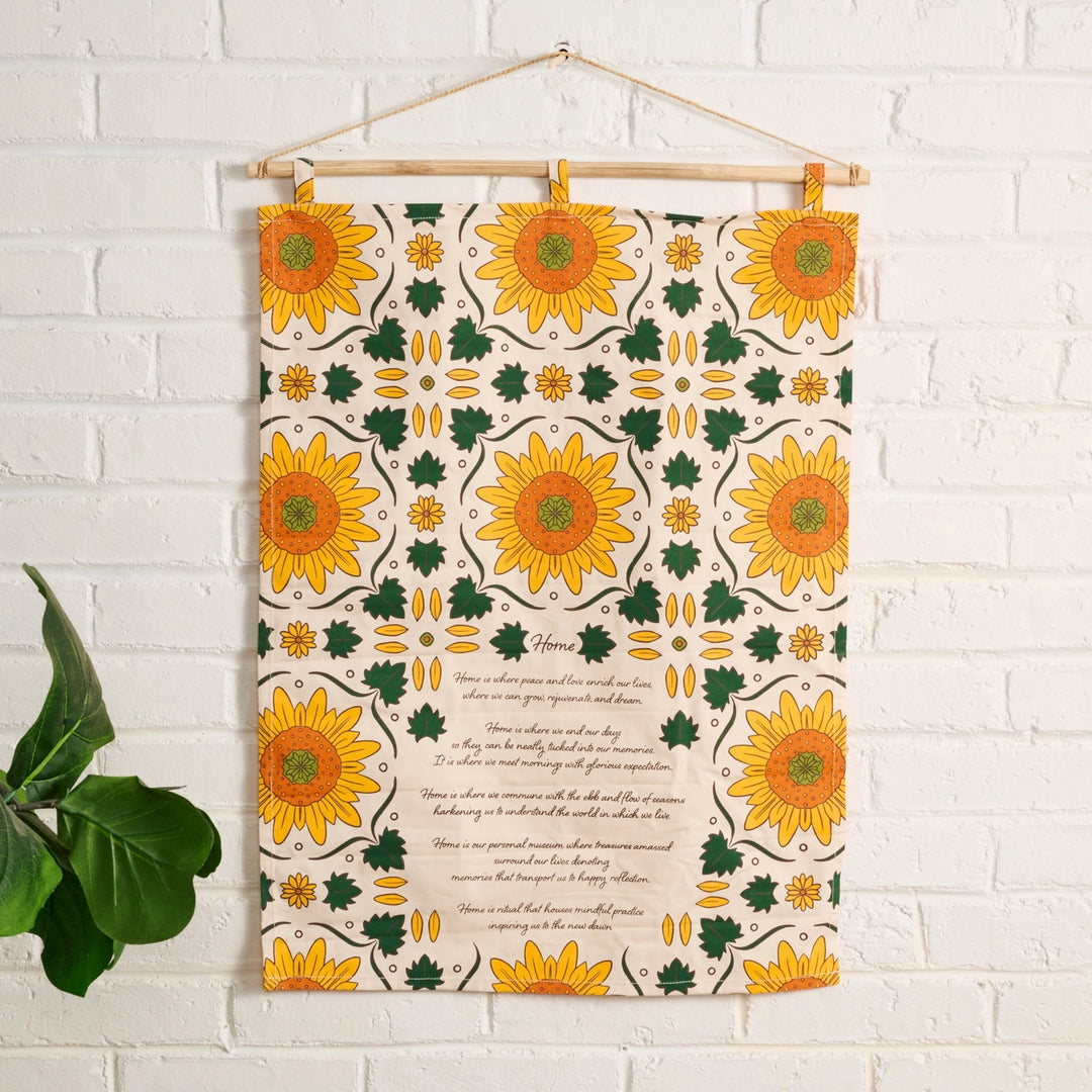 Decorative wall hanging with sunflower pattern and poem on a white brick wall.