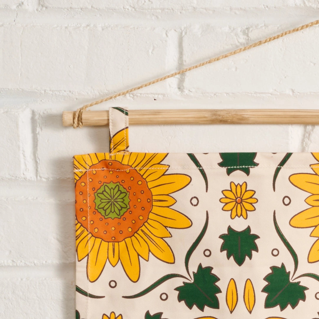 Decorative banner with sunflower pattern hanging against a white brick wall.