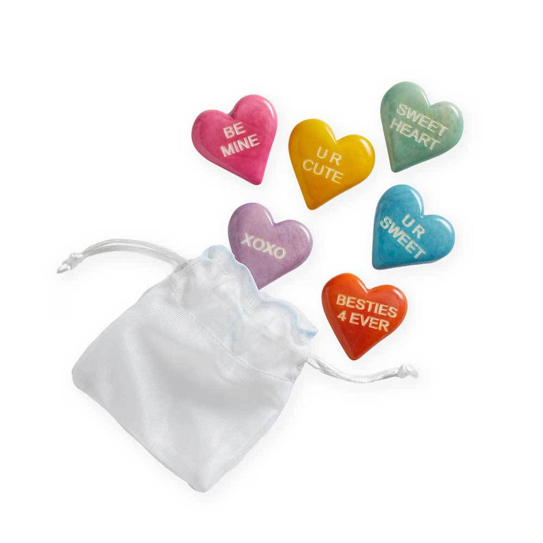 Colorful heart-shaped tagua tokens with messages on a white drawstring bag.