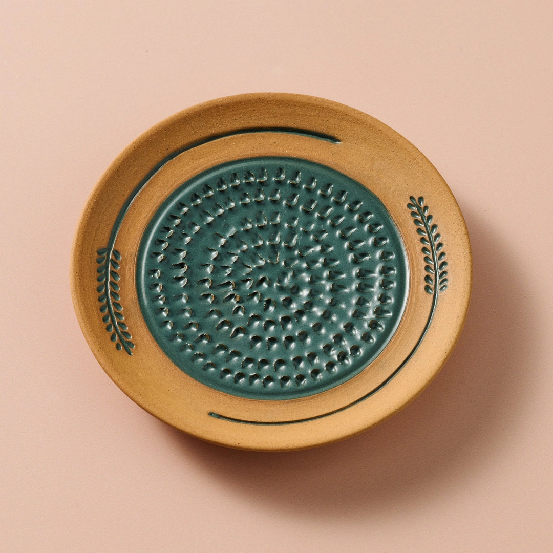 Ceramic grater with green center and beige rim on a tan background