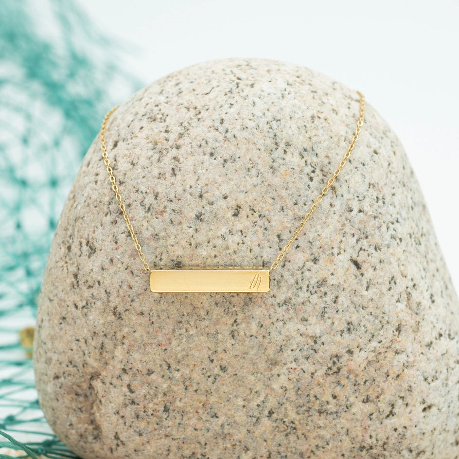 Gold necklace on a textured stone surface with a blurred green background