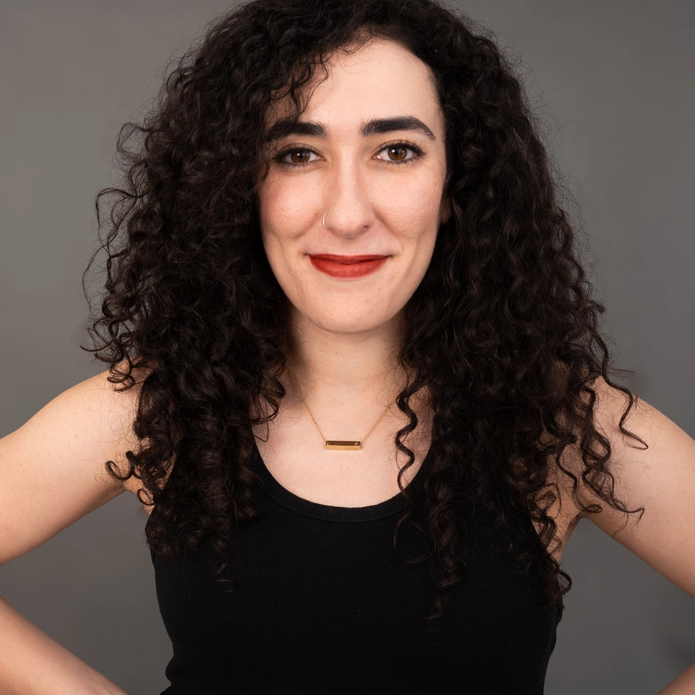 Woman with curly hair wearing a black top against a gray background