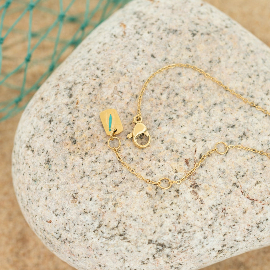 Gold necklace on a textured stone surface with a blurred natural background