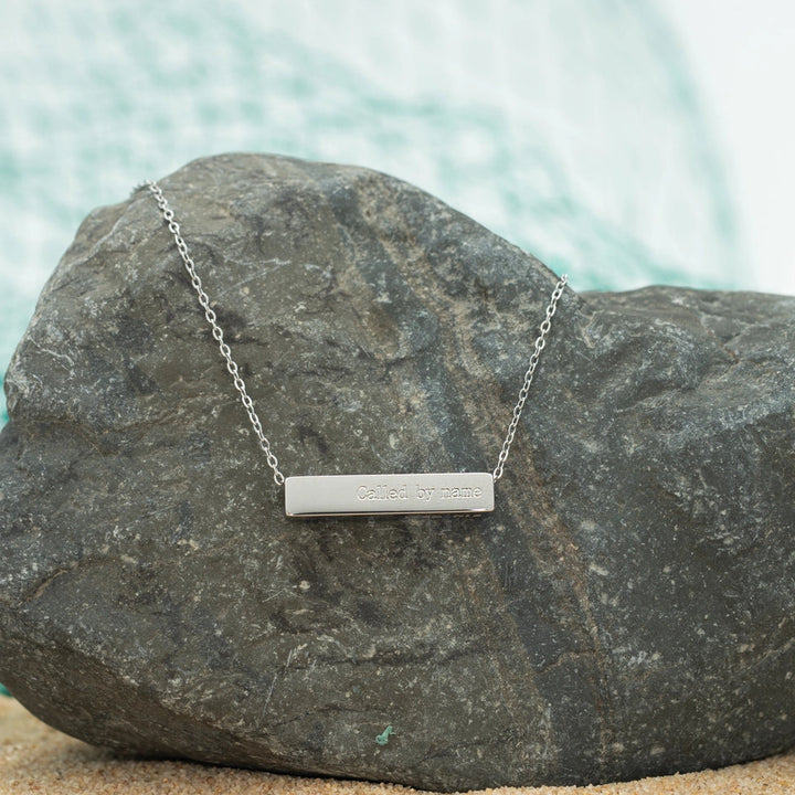 Silver bar necklace on a rock with water in the background