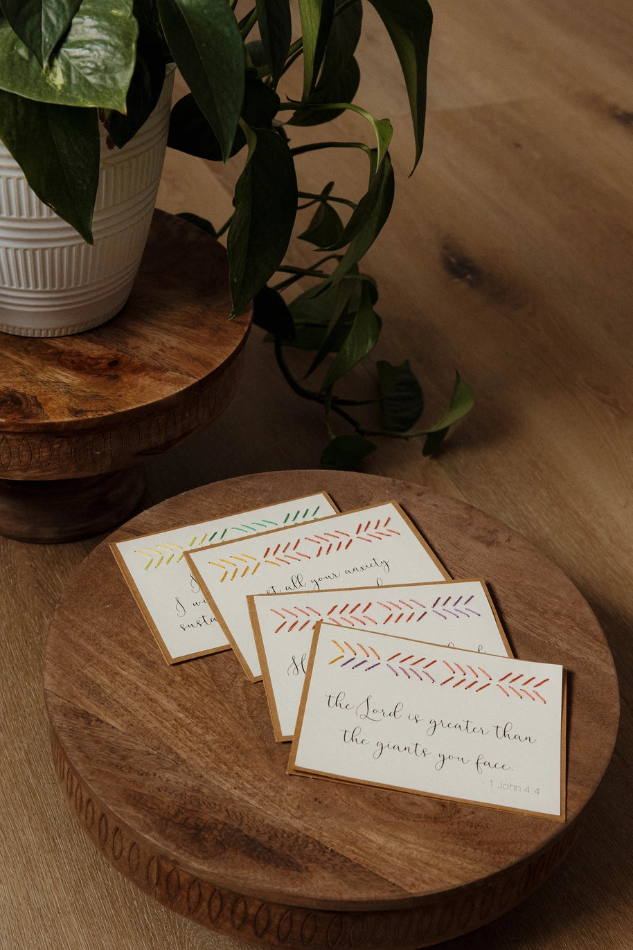 Set of cards with decorative designs on a wooden surface with a plant in the background