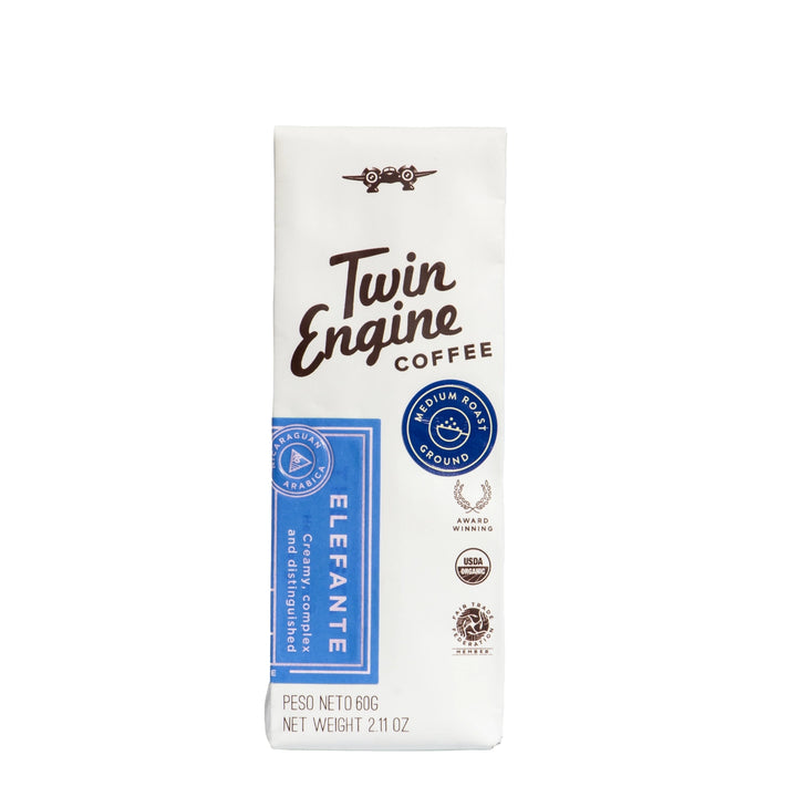 A package of Twin Engine Coffee Elefante medium roast ground coffee, shown on a plain white background. The packaging is primarily white with dark brown text and a blue vertical label on the left side.