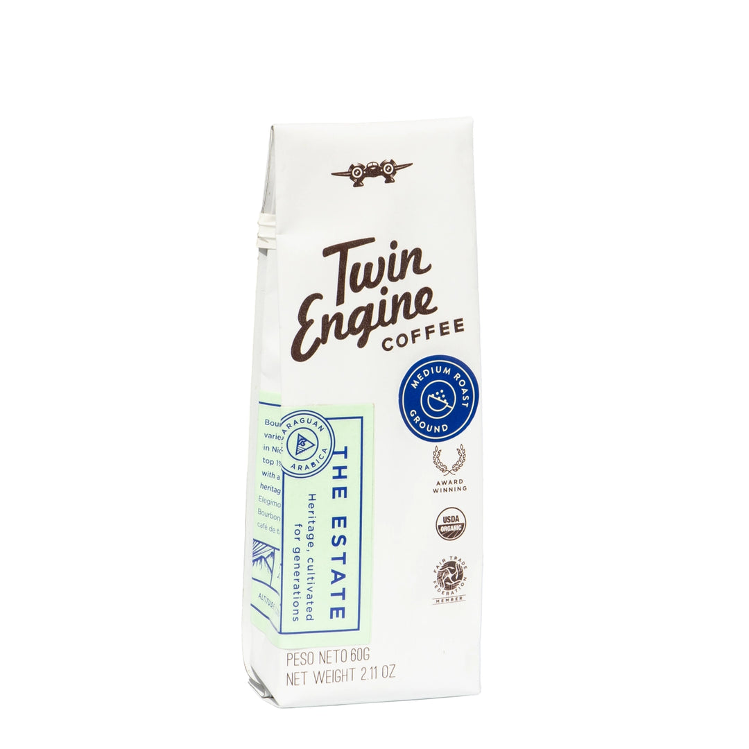 A 600g bag of Twin Engine Coffee from The Estate, featuring a white paper bag with brown script lettering, a blue circular seal, and various certification logos on a plain white background.