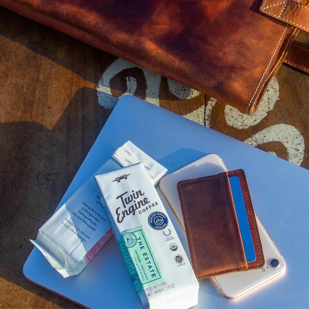 Two Twin Engine coffee packets on a blue surface with a brown leather wallet and phone.