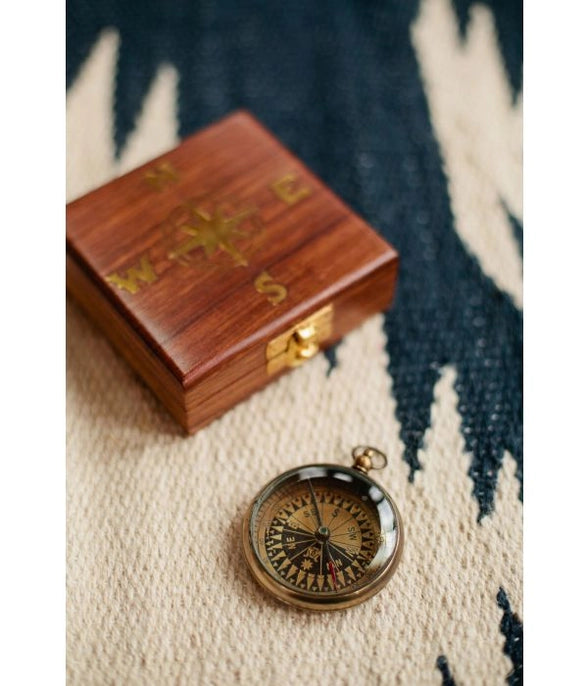 Vintage-style compass on a textured surface with a wooden box in the background