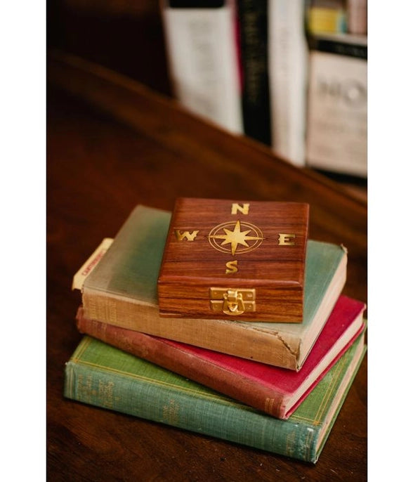Wooden compass box on top of vintage books with a blurred bookshelf in the background