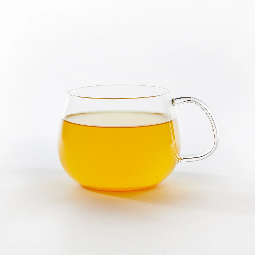 Clear glass mug with handle filled with turmeric ginger tea on a white background