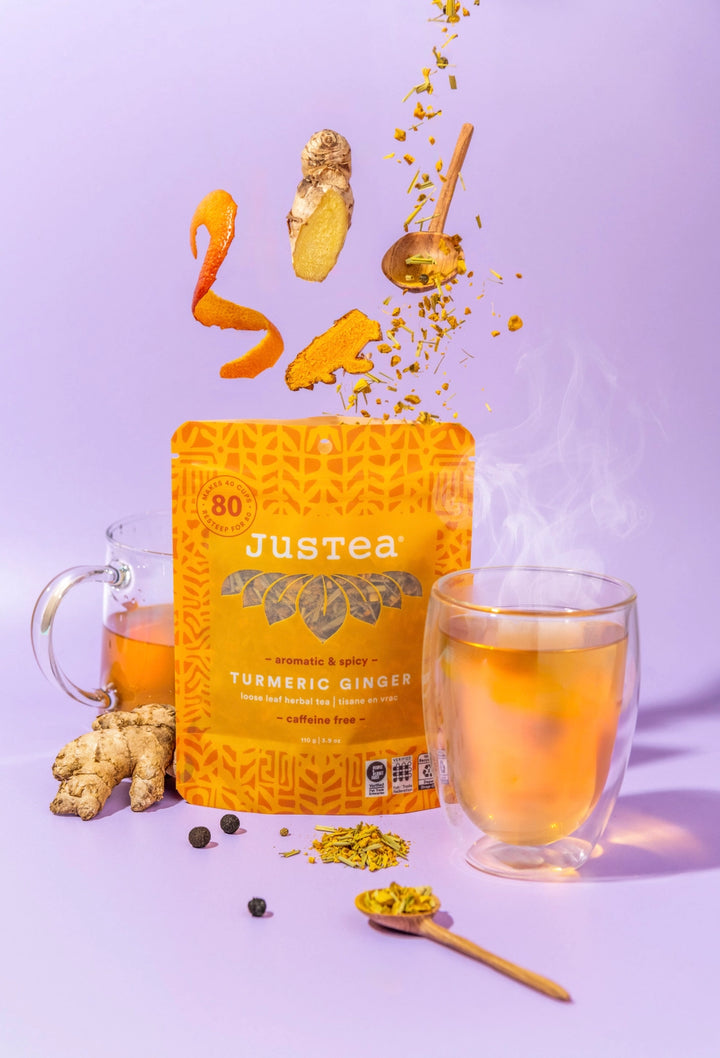 Justea Turmeric Ginger tea packaging with a glass of tea and ginger roots on a purple background