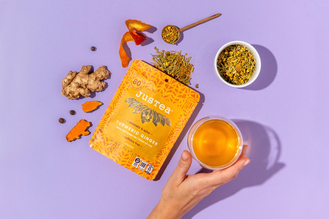 Jureea tea tumeric ginger packaging with a cup of tea, dried herbs, and a spoon on a purple background
