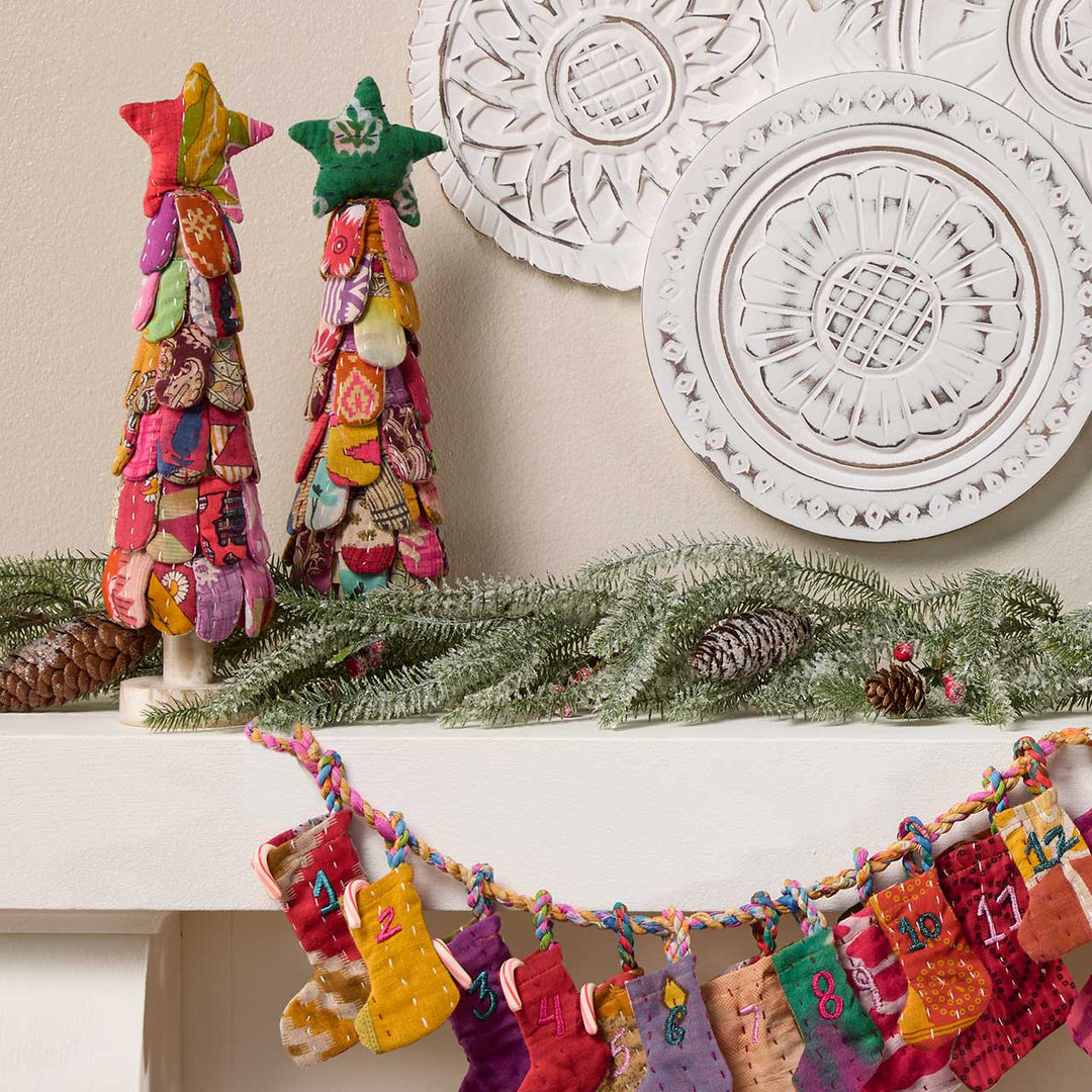 Decorative Christmas mantel with colorful star trees and a bunting against a neutral wall.
