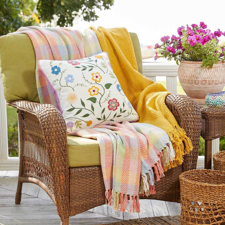 Wicker chair with colorful blankets and a floral pillow on a patio