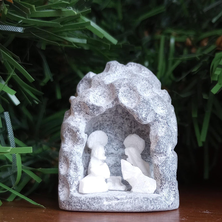 Small alabaster nativity scene set against a green foliage background.