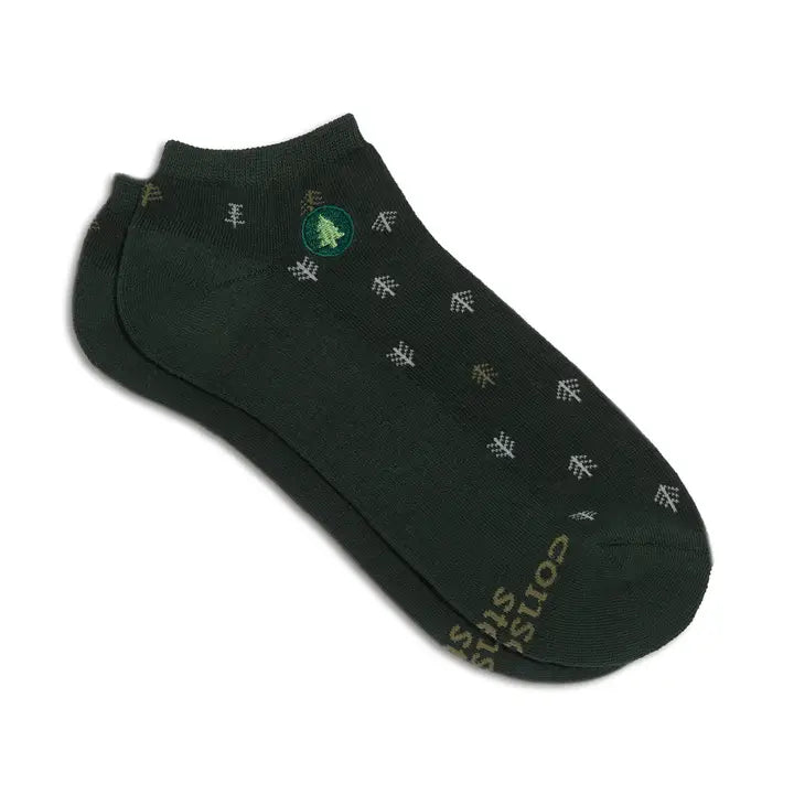 A pair of low-cut ankle socks in dark forest green, featuring a repeating pattern of small white pine tree silhouettes and a green circular logo near the cuff. The brand name 'consist' is printed in gold on the toe area.