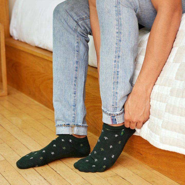 Person wearing green socks with a tree pattern, sitting on a bed.