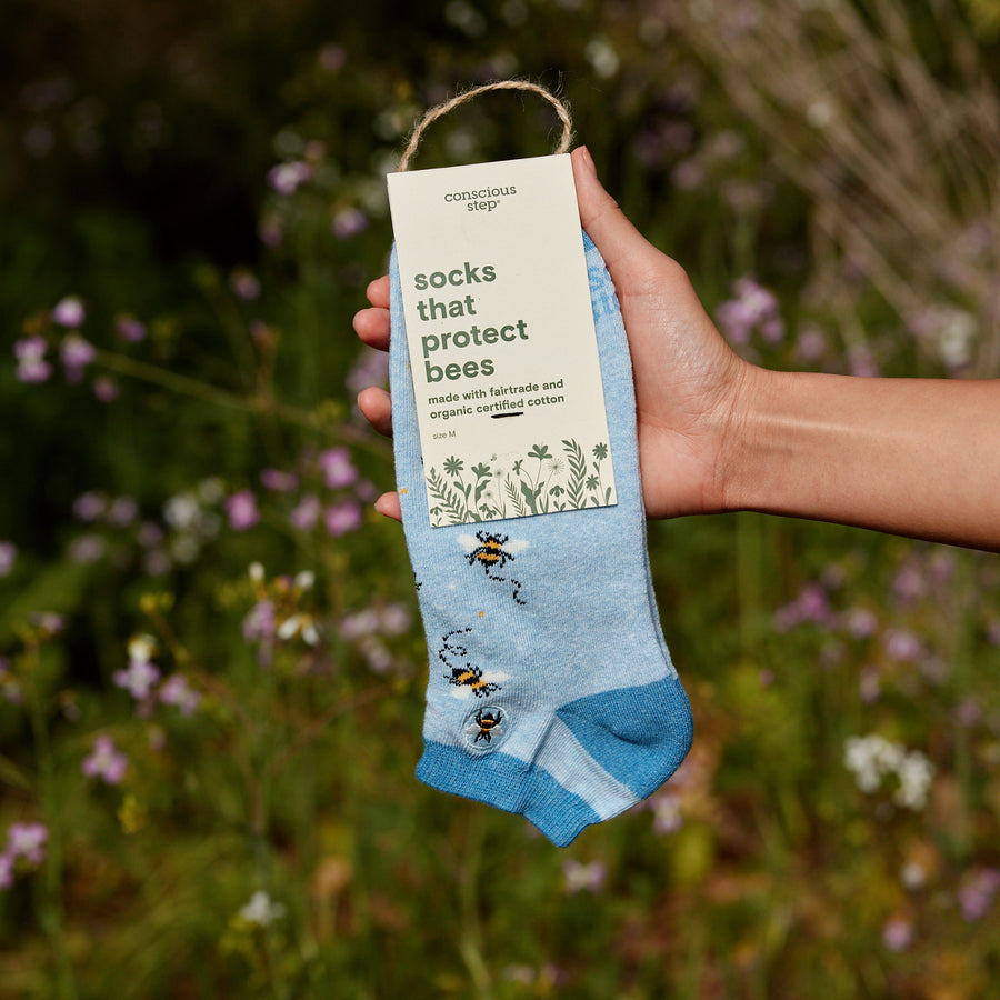 Hand holding a pair of blue socks with bee design and a visible label against a natural background.