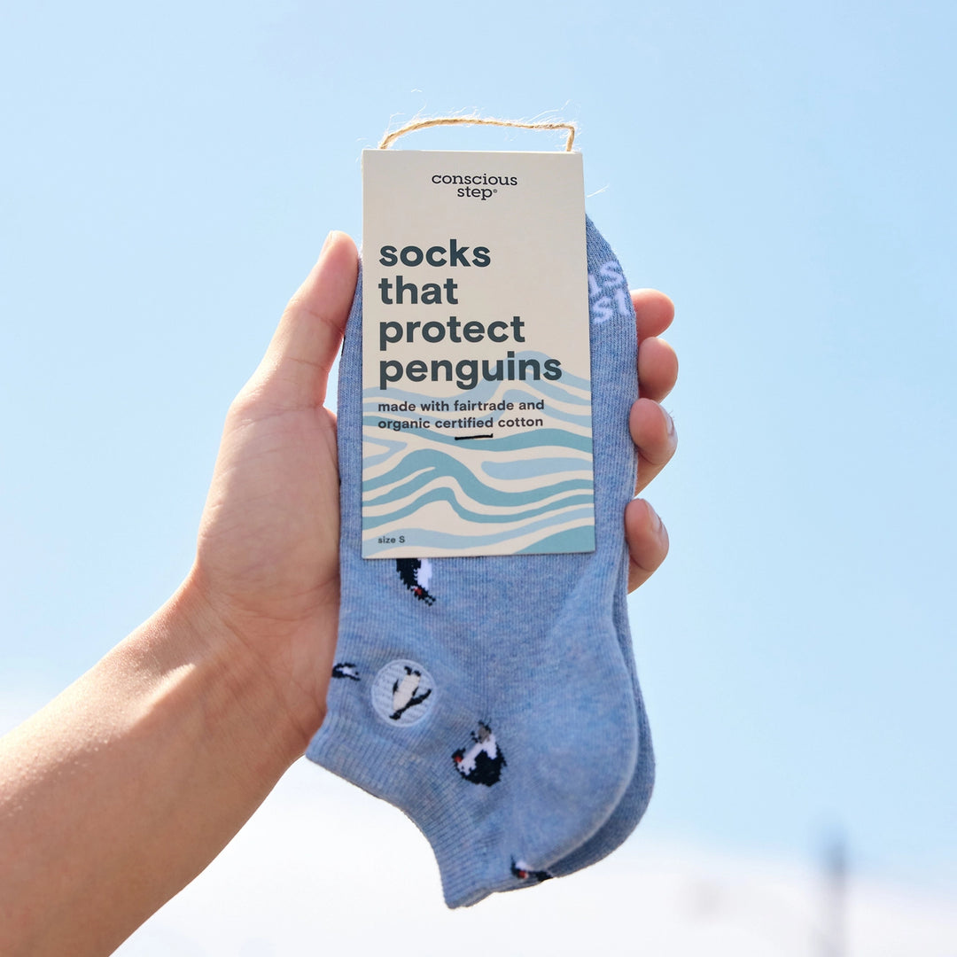 Hand holding a pair of socks with a label indicating they protect penguins against climate change.