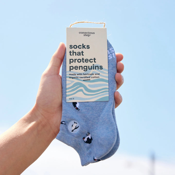 Hand holding a pair of socks with a label indicating they protect penguins against climate change.
